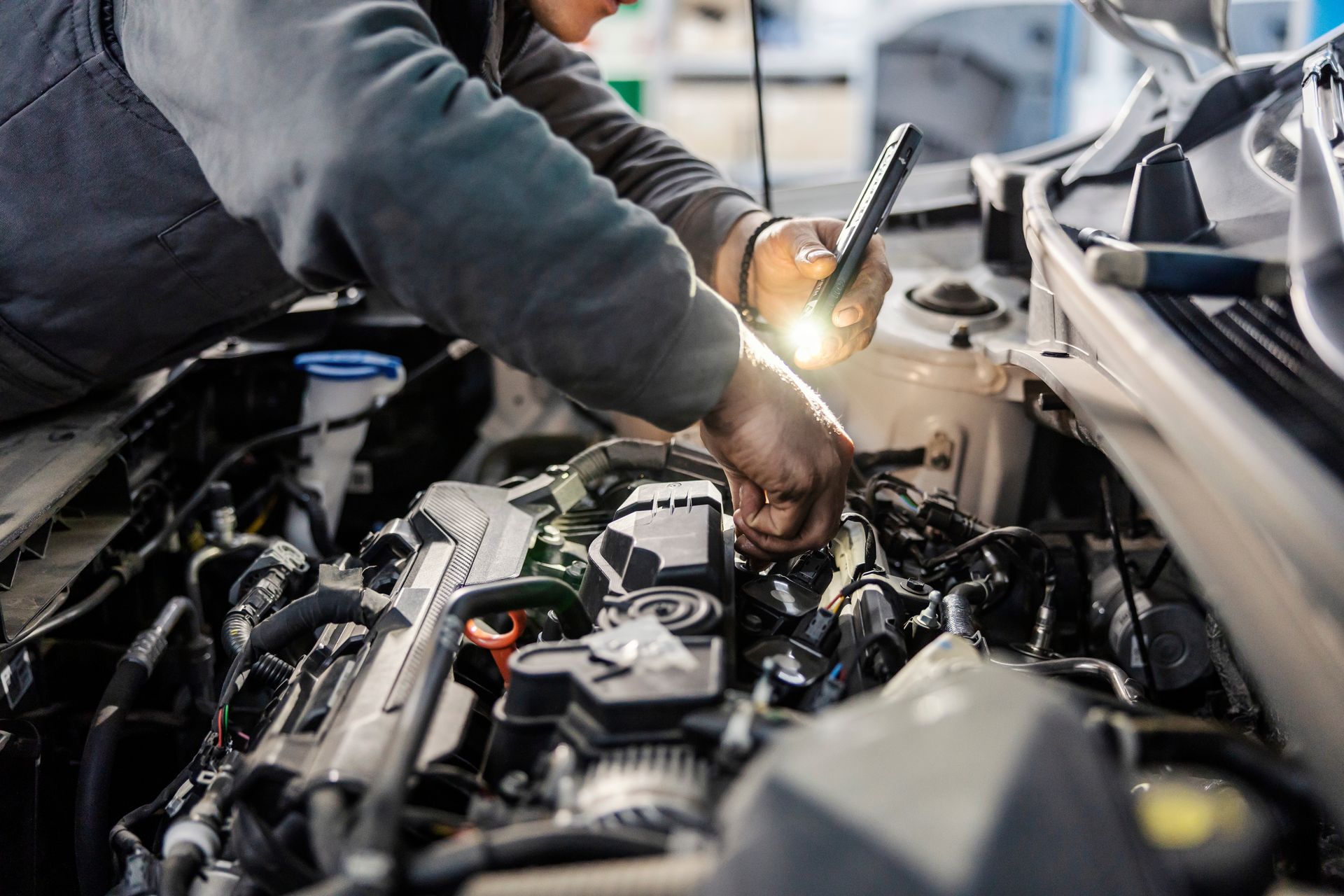 Mechanic working under a car hood in a garage, using a tool with a bright work light