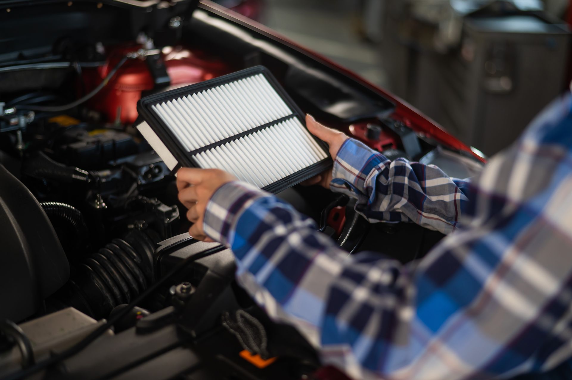 Person holding a new air filter in front of a car engine in a garage.