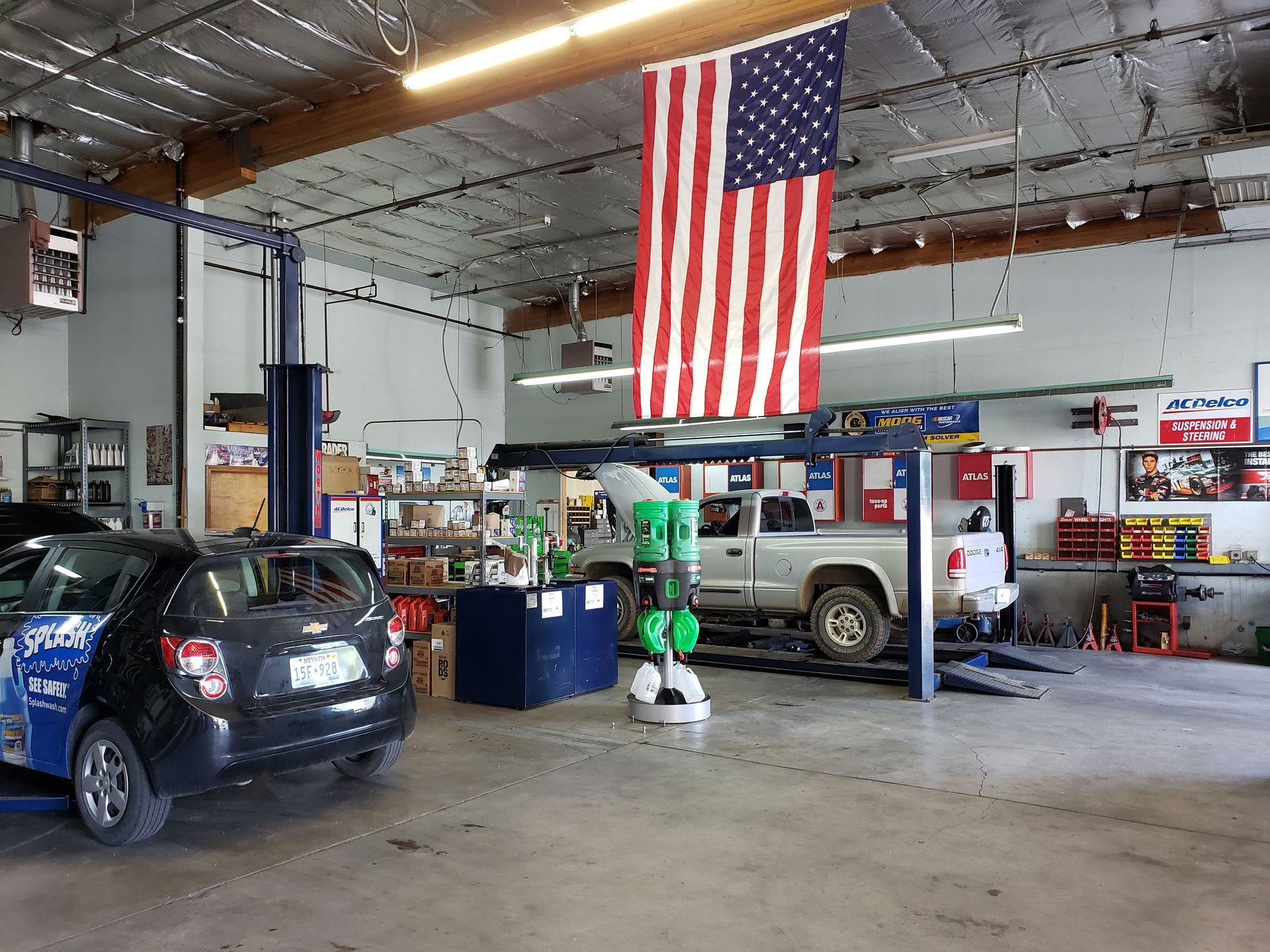 Car repair shop with American flag, two vehicles on lifts, tools, and supplies.