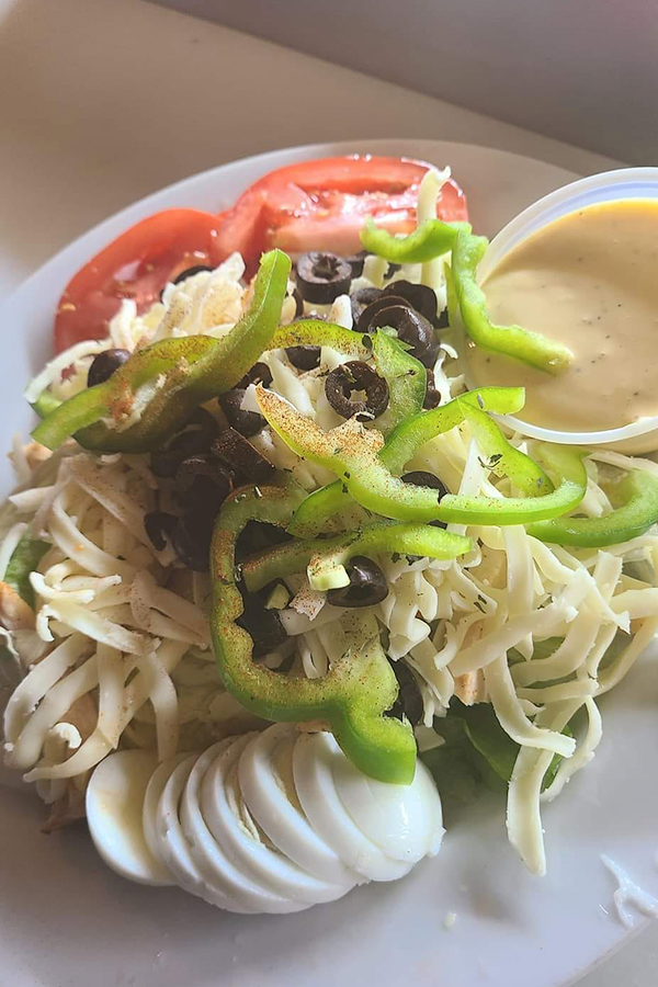 A close up of a salad with eggs , peppers , olives and tomatoes on a plate.