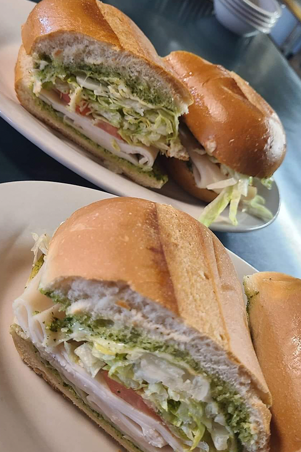 Two hot grinder sandwiches are sitting on a white plate on a table.