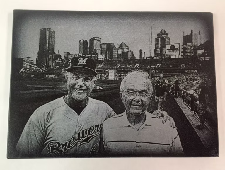 Two smiling men in baseball attire posed before a city skyline and stadium backdrop