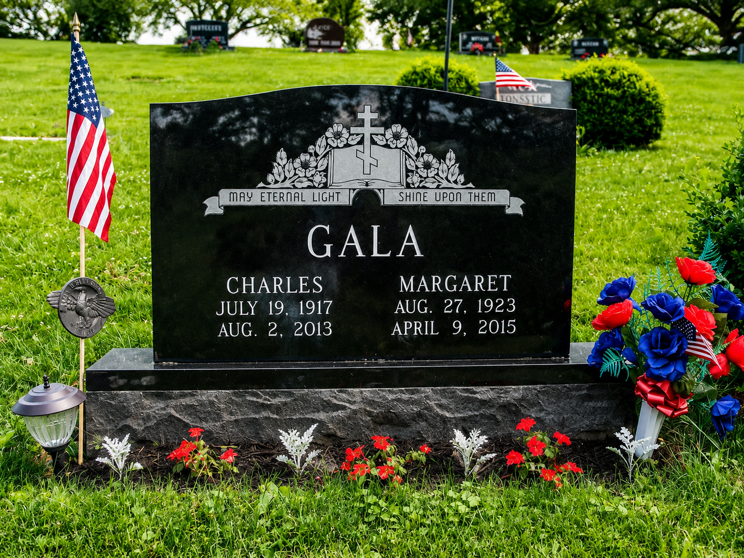 Black memorial headstone with flowers and American flags in a grassy cemetery garden