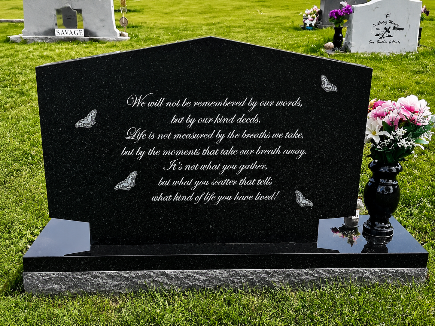 Black gravestone with white script and butterfly accents in a cemetery, with pink flowers beside it