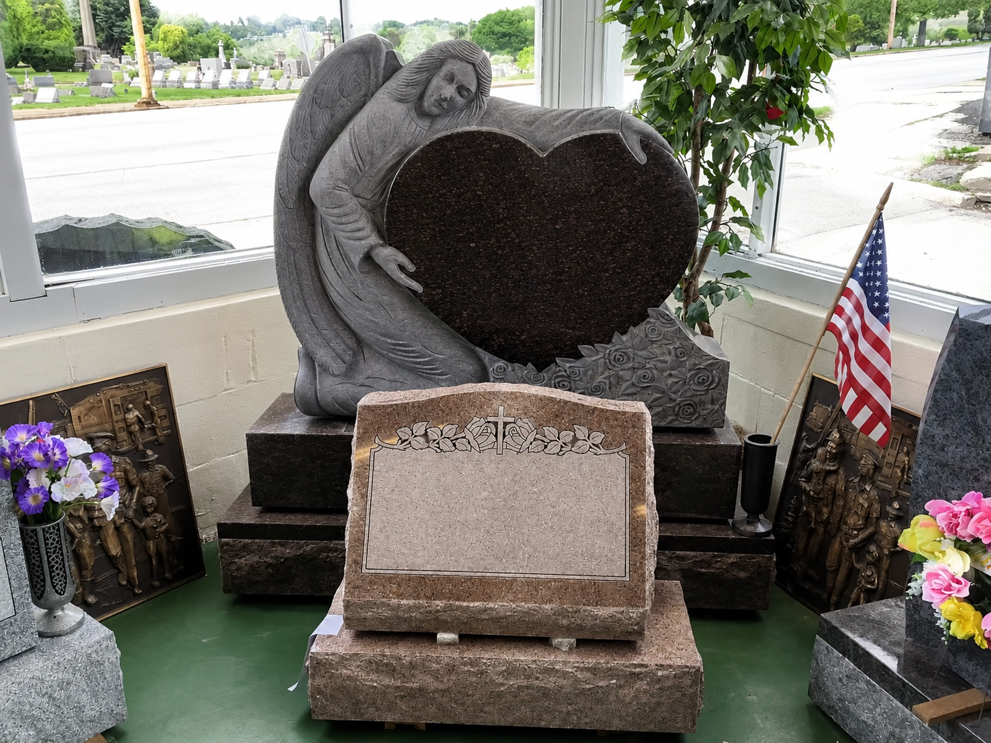 Memorial stone with heart-shaped centerpiece and small American flag, surrounded by flowers on a porch.