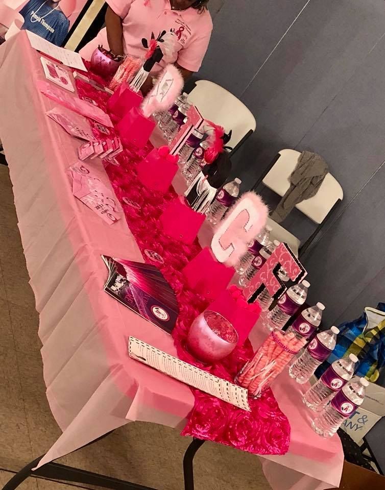 Pink-decorated party table with cakes, bottles, gifts, and signs at an indoor celebration