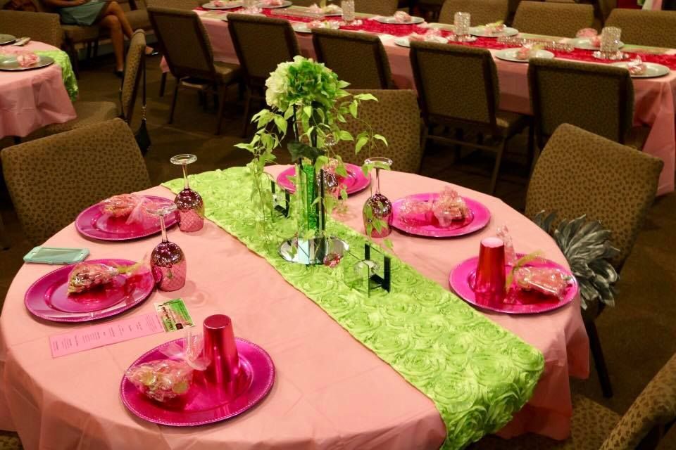 Decorated banquet table with pink place settings and a green centerpiece runner in a dining hall