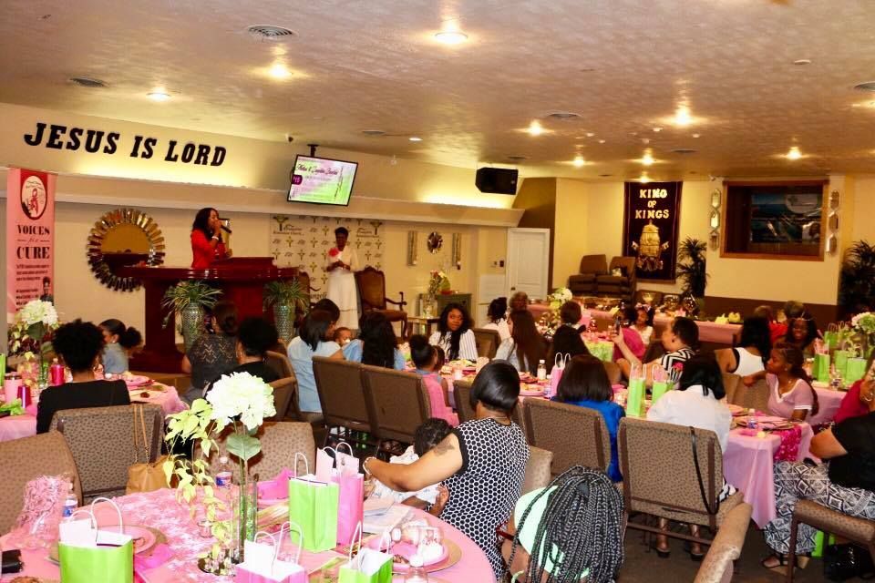 Church banquet with guests seated at pink-decorated tables under a “JESUS IS LORD” sign
