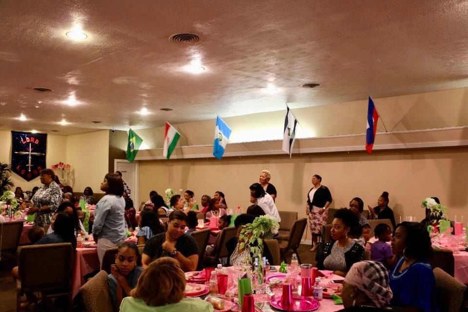 Banquet hall with people dining at round tables, pink decorations, and flags hanging along the wall