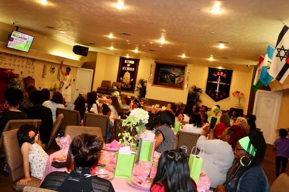 Crowded indoor banquet hall with seated guests at tables, warm lighting, and flags on the walls