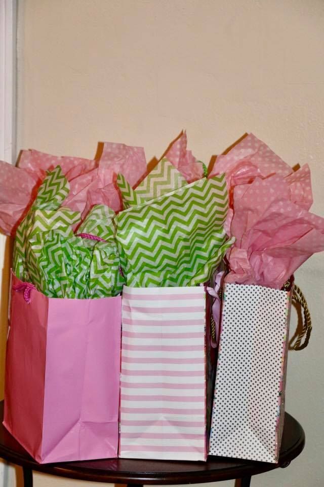 Three colorful gift bags with tissue paper on a table against a beige wall