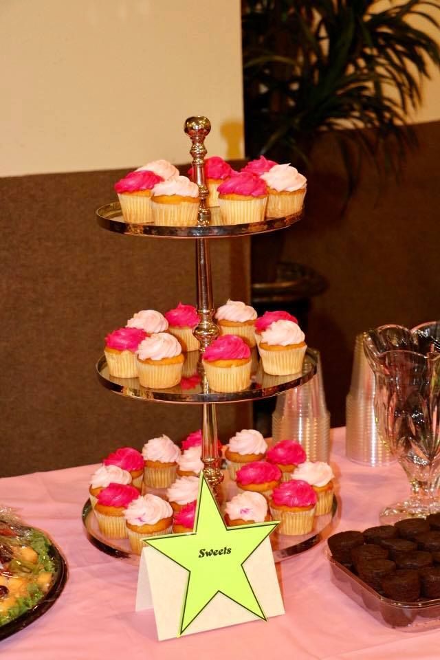 Tiered stand of pink and yellow cupcakes with a green star label on a table.