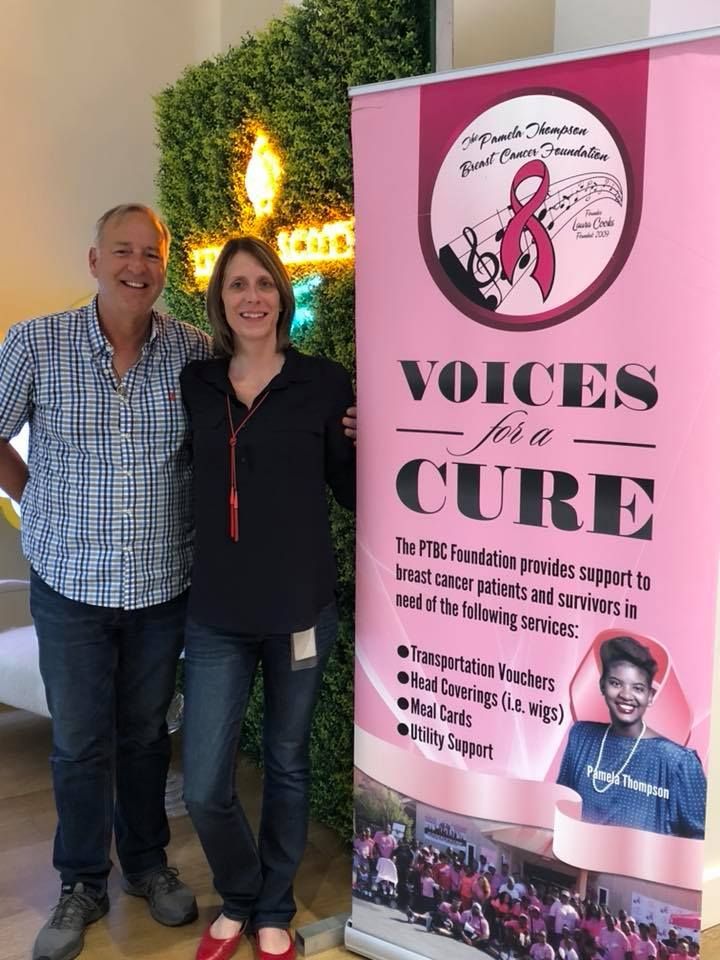 Two people standing beside a pink “Voices for the Cure” banner at an indoor event.