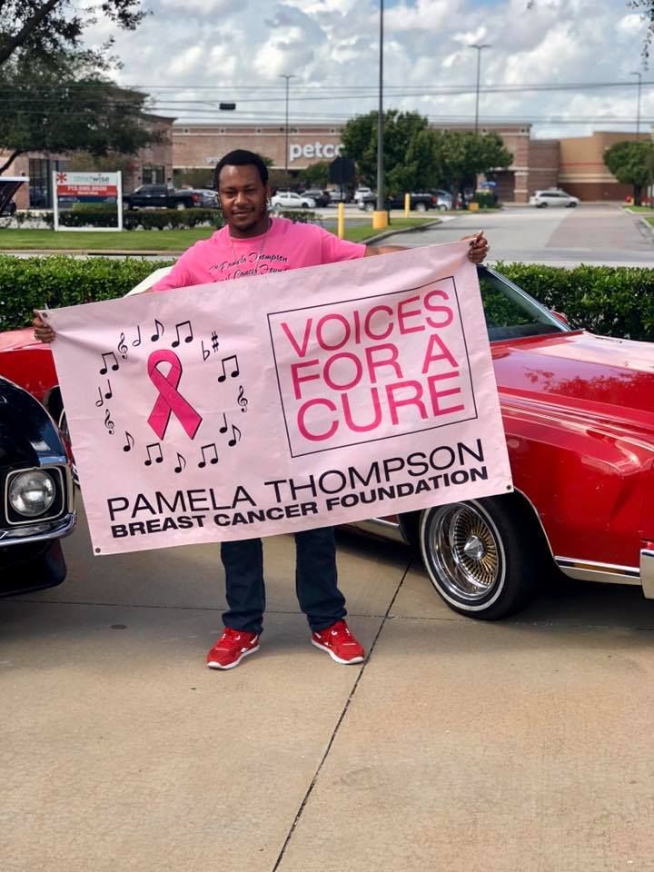Person holding a “Voices for a Cure” Pamela Thompson Breast Cancer Foundation banner beside a red car.