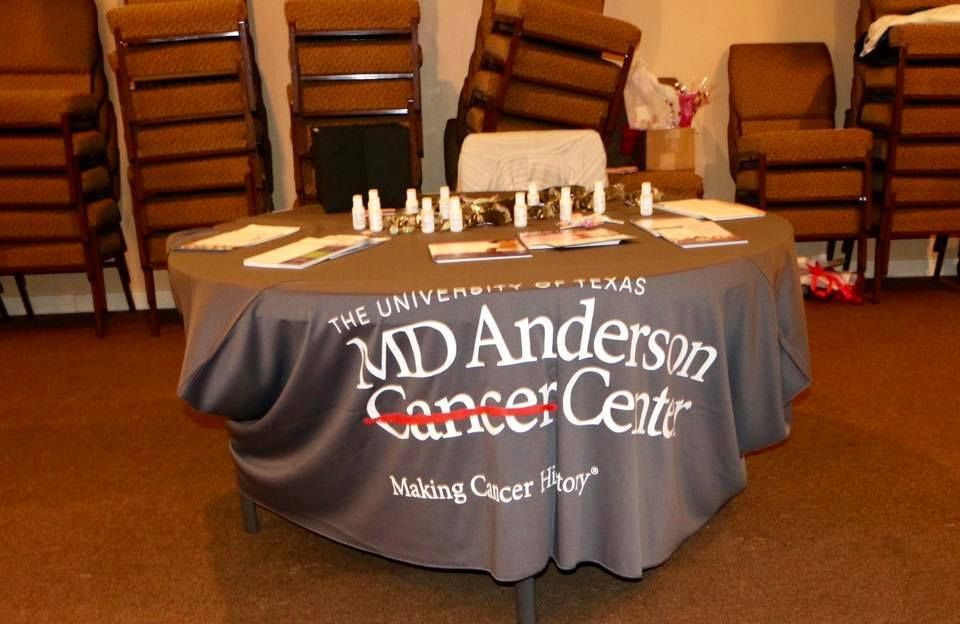 Donation table with gray cloth for Anderson Cancer Center in a room with stacked chairs and papers on top