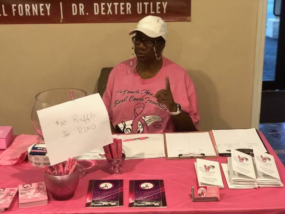 Woman at a pink table displaying books and flyers at an indoor event.