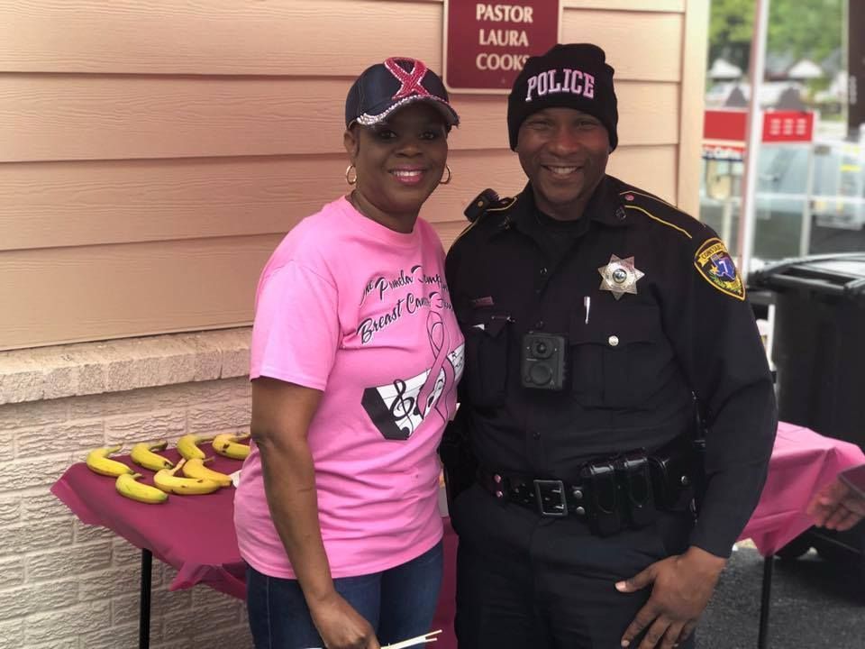 Smiling police officer and woman posing beside a table with pink cupcakes at a community event.