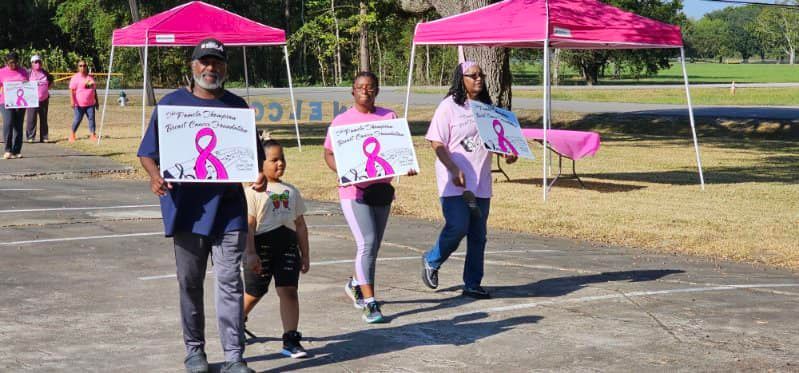 People walking outdoors holding pink ribbon signs near bright pink tents at a breast cancer awareness event