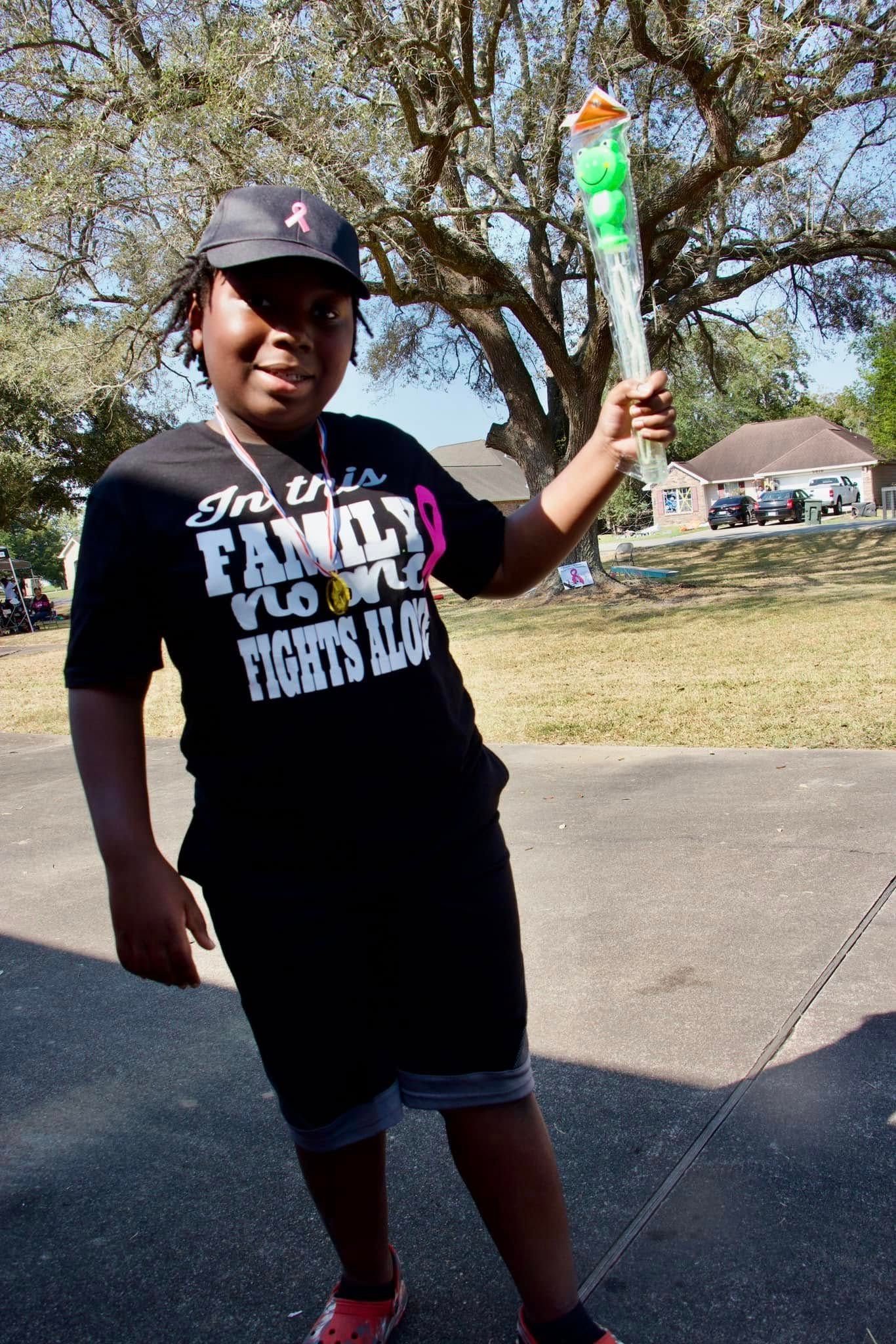 Person standing outdoors on a driveway, holding a colorful toy wand and wearing a black T-shirt and cap.