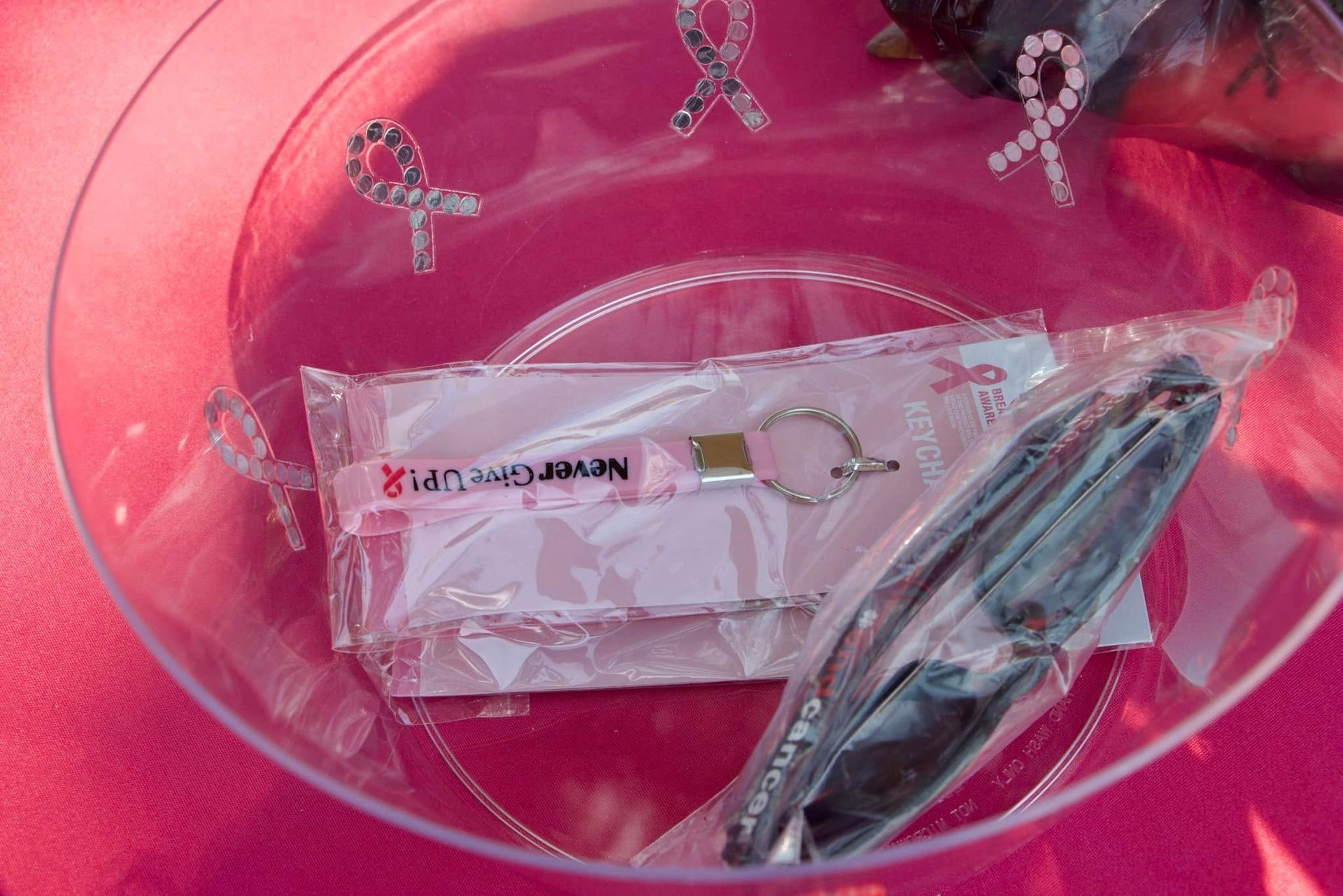 Clear bowl on pink cloth holding a wrapped item and a pair of tweezers or tongs.