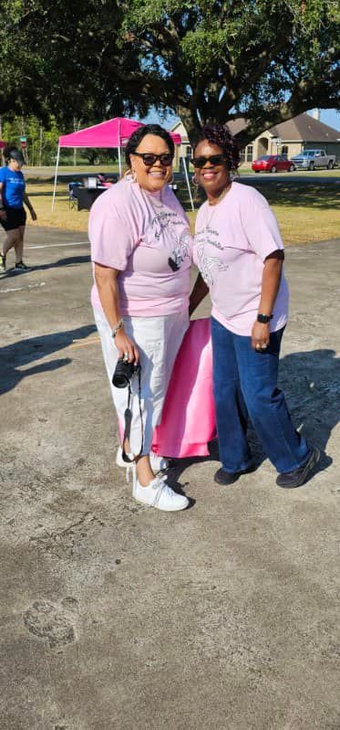 Two people in pink shirts and sunglasses pose outdoors on a sunny day.