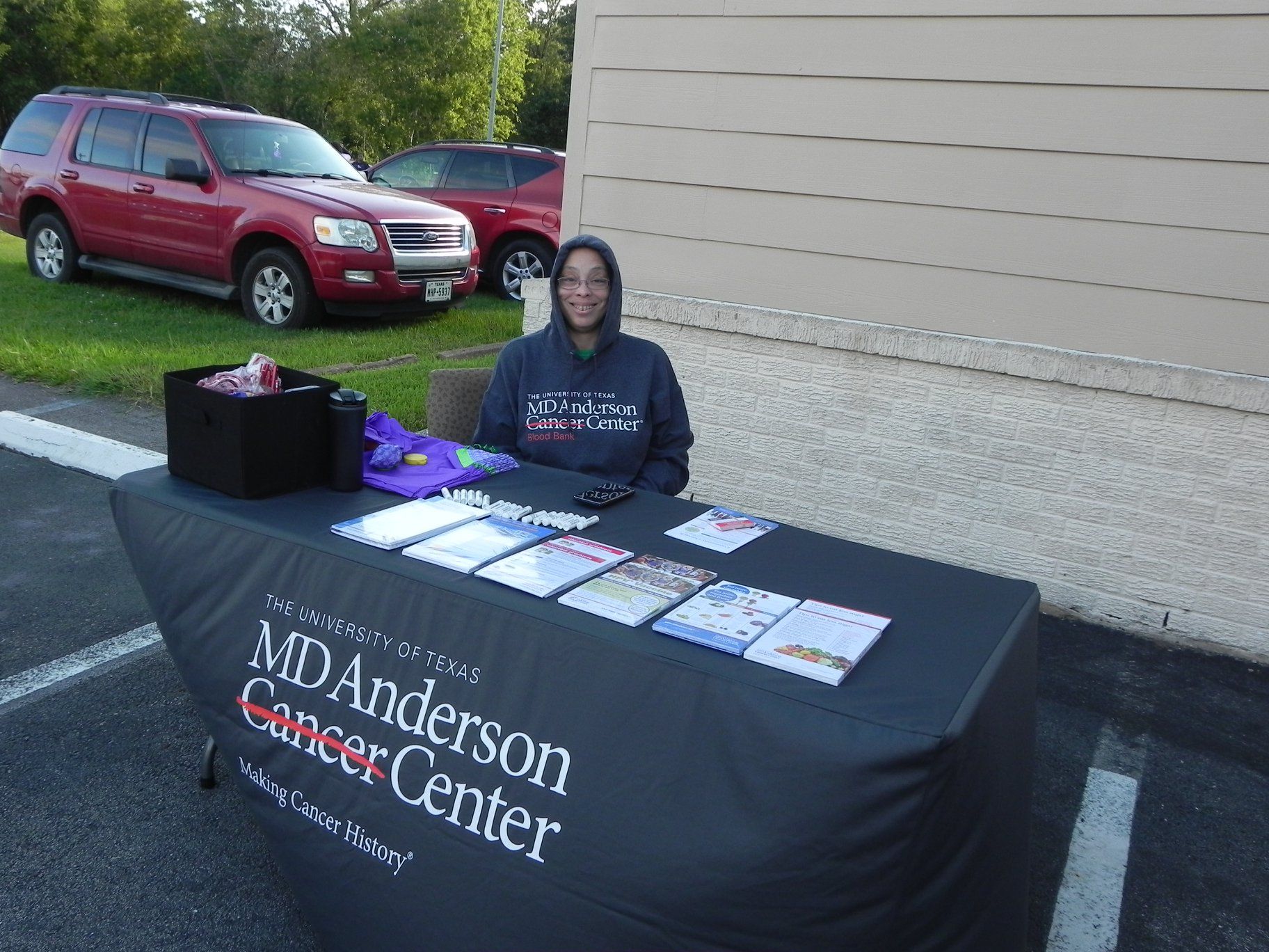 Woman seated at a M.D. Anderson Cancer Center outreach table with brochures and forms outdoors