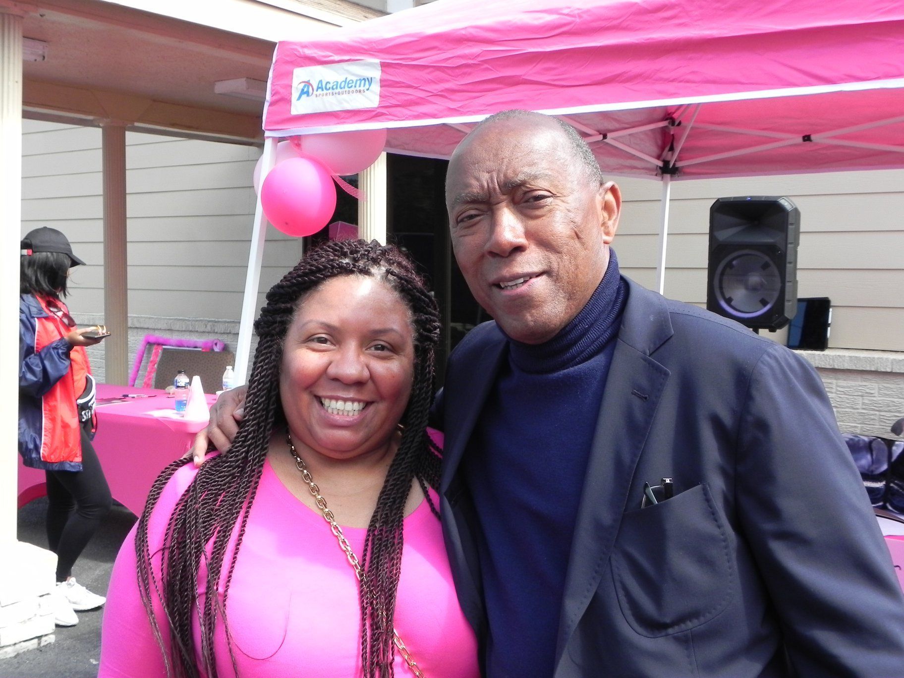 Two smiling people standing together under a pink canopy at an outdoor event.