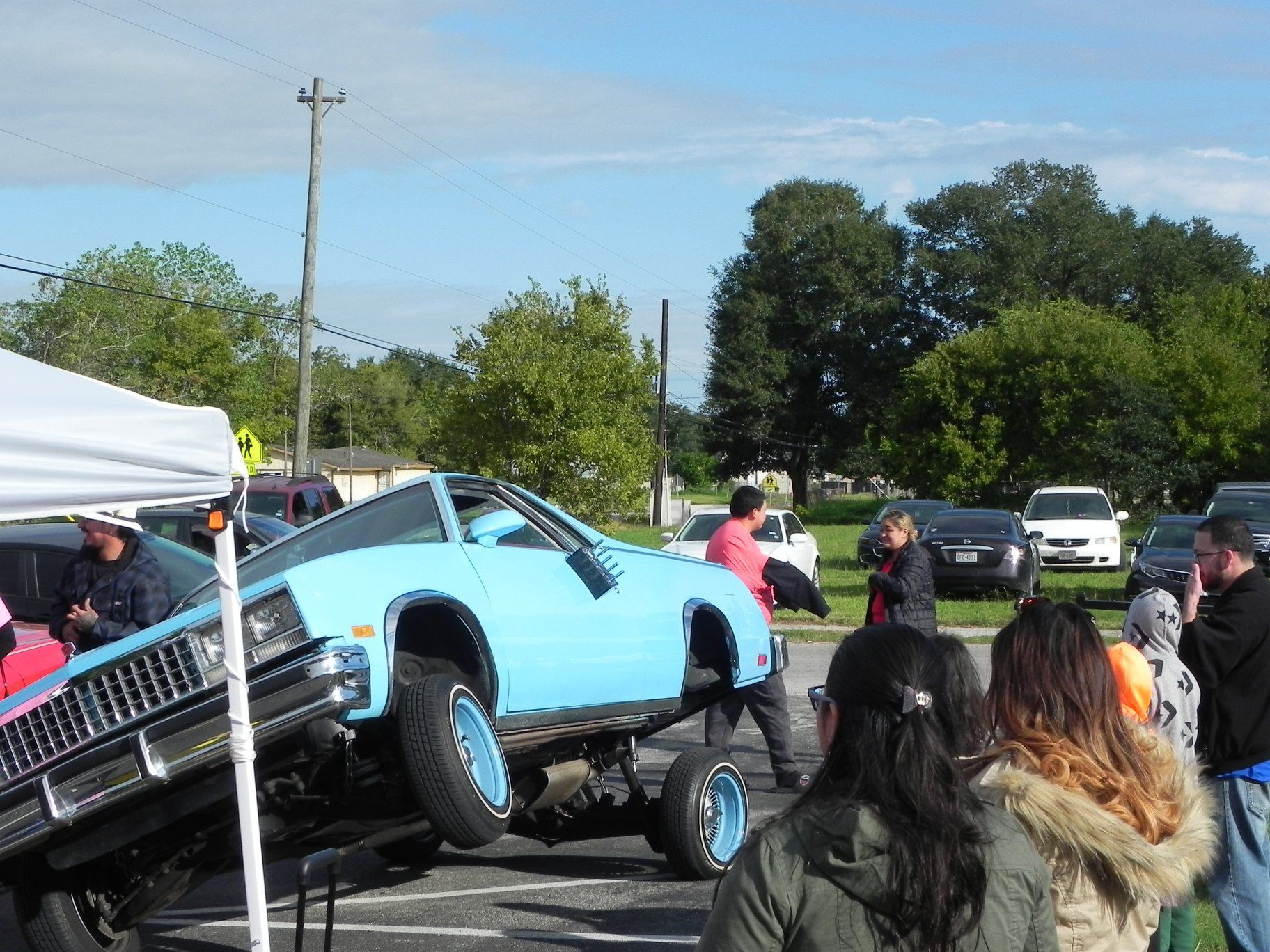Blue car tilted on a trailer at an outdoor car show, with people gathered around.