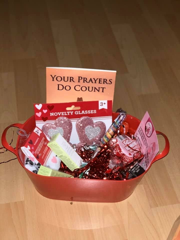 Red gift basket with novelty glasses, candy, and a sign reading “Your prayers do count”
