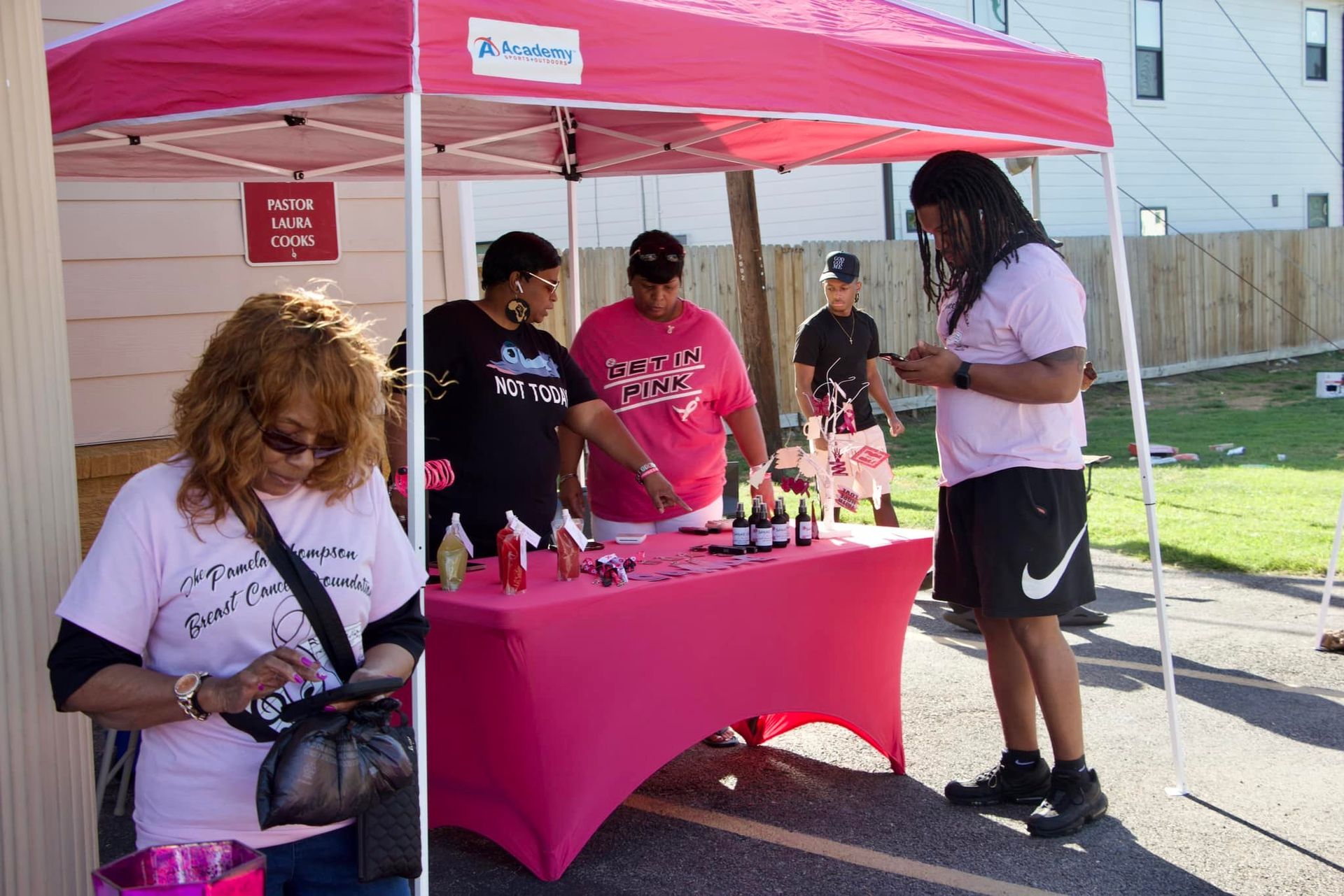 People at a pink canopy table handing out items outdoors in a parking lot