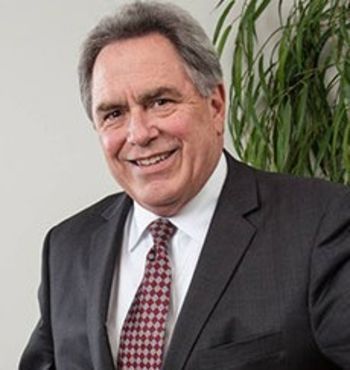 Man in suit smiling; indoor setting with greenery.