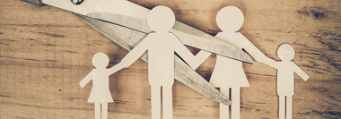 Scissors cutting a paper family, representing family separation or divorce on a wood background.