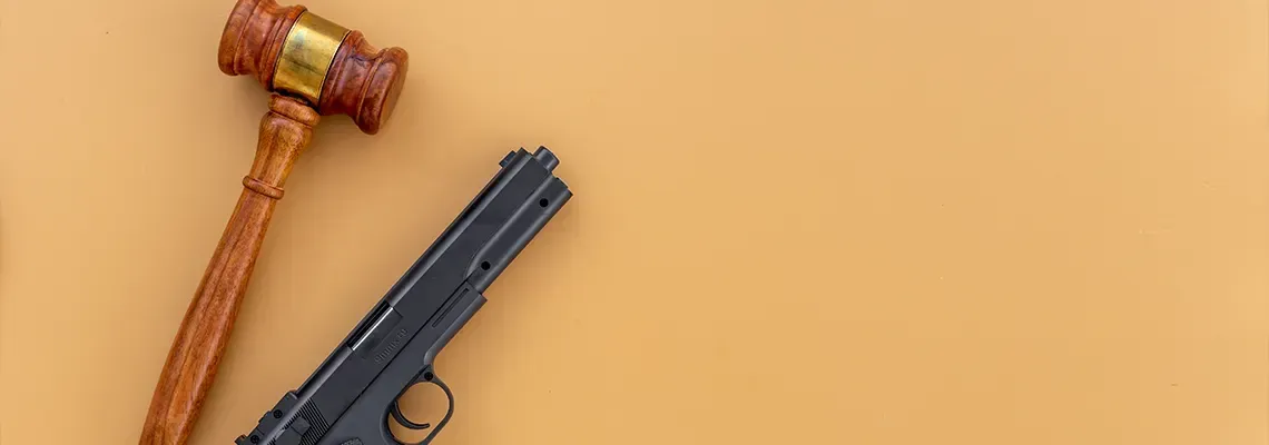 Wooden gavel and black handgun on a tan background.
