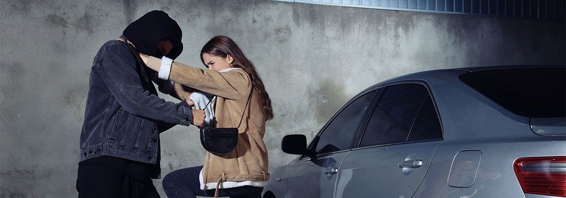 Person in hoodie and mask detaining a woman near a car at night.