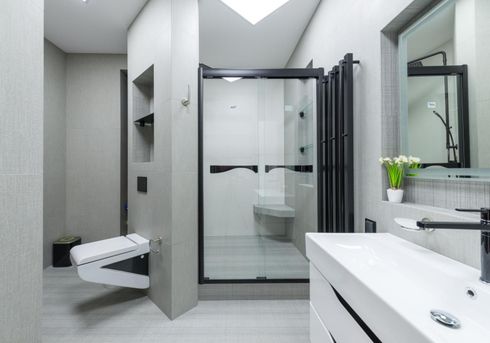 Modern accessible bathroom with walk-in shower, toilet, sink, mirror, and light gray tile.