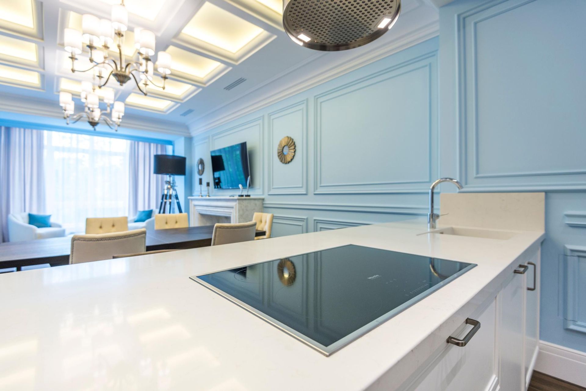 Bright blue modern kitchen with white island, built-in cooktop, and large windows near a dining area