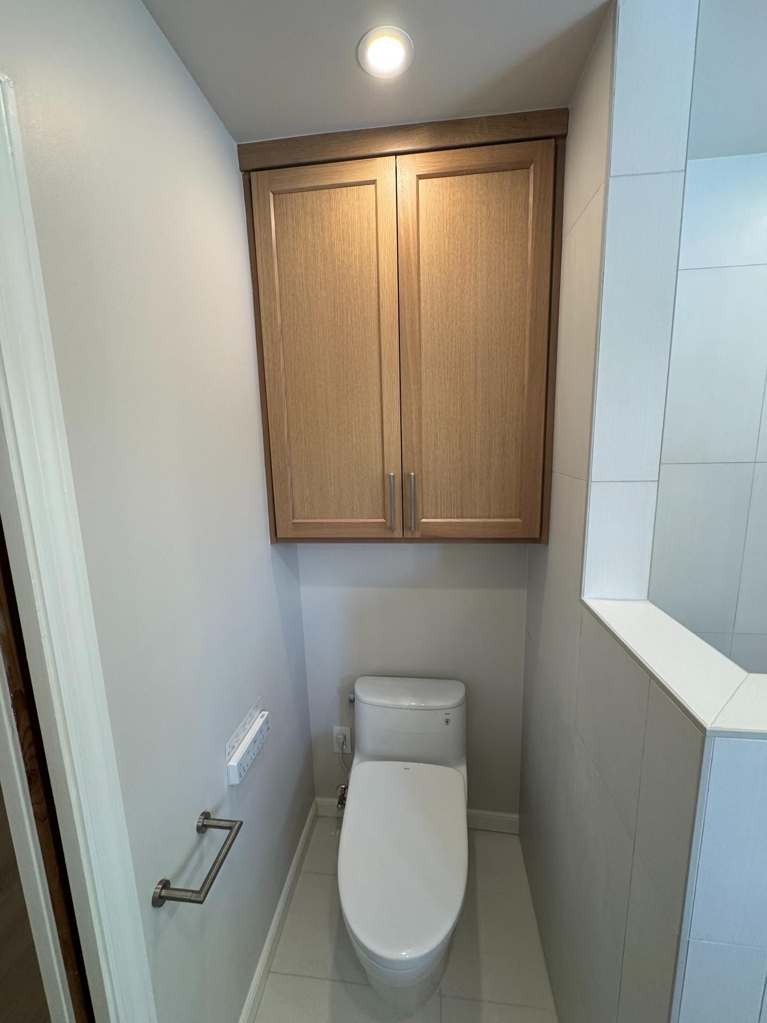 Small narrow restroom with a toilet and wooden cabinet above it.