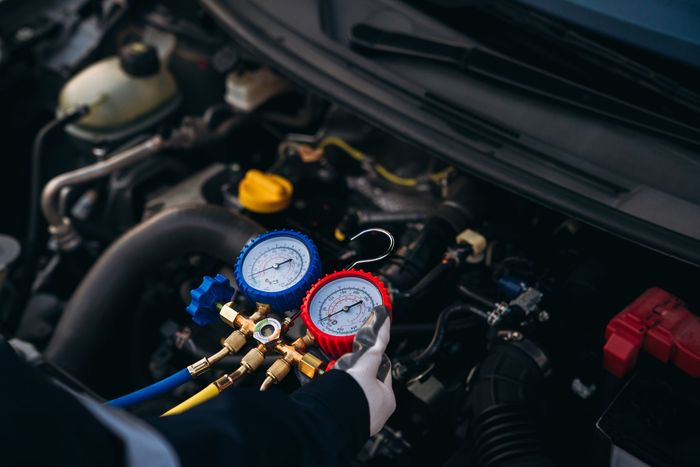 Mechanic using pressure gauges to inspect a car engine in an open hood compartment | Elite Auto Repair & Service Inc