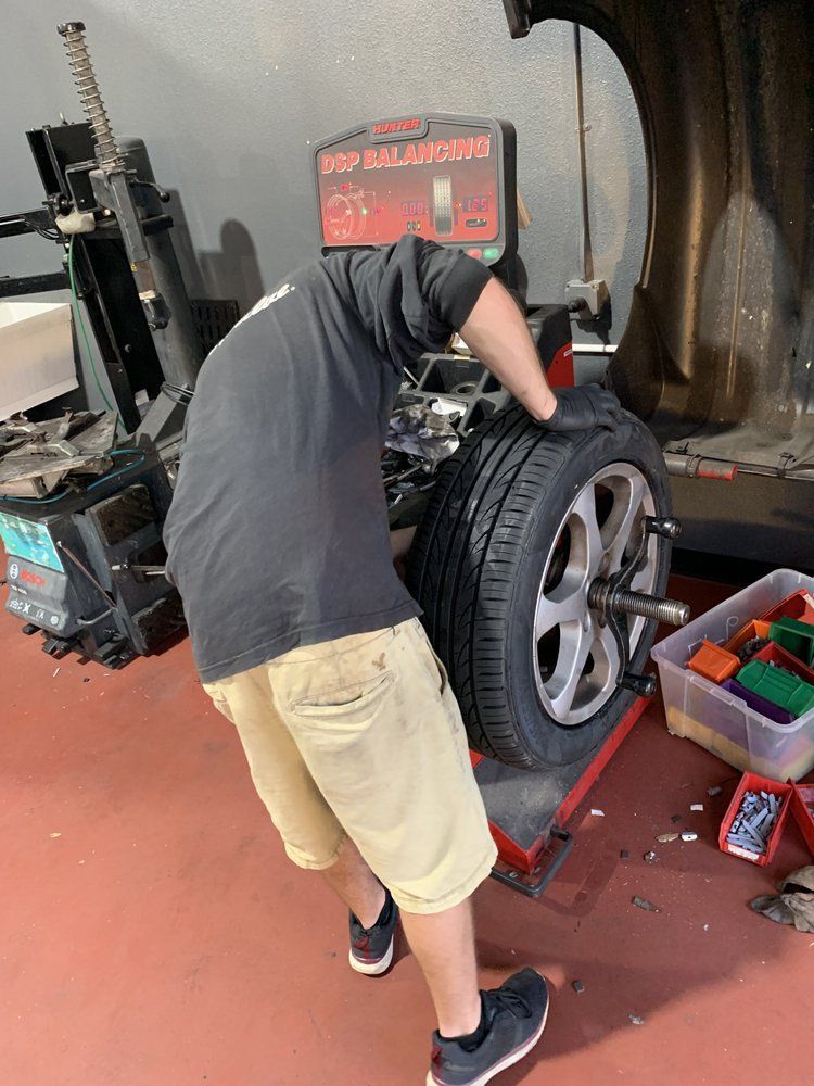 Person changing a car tire at an auto shop beside a tire machine and tool cart | Elite Auto Repair & Service Inc