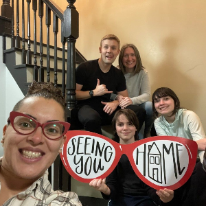 Group posing on stairs with red heart signs reading “I am” and “feel loved,” smiling at the camera.
