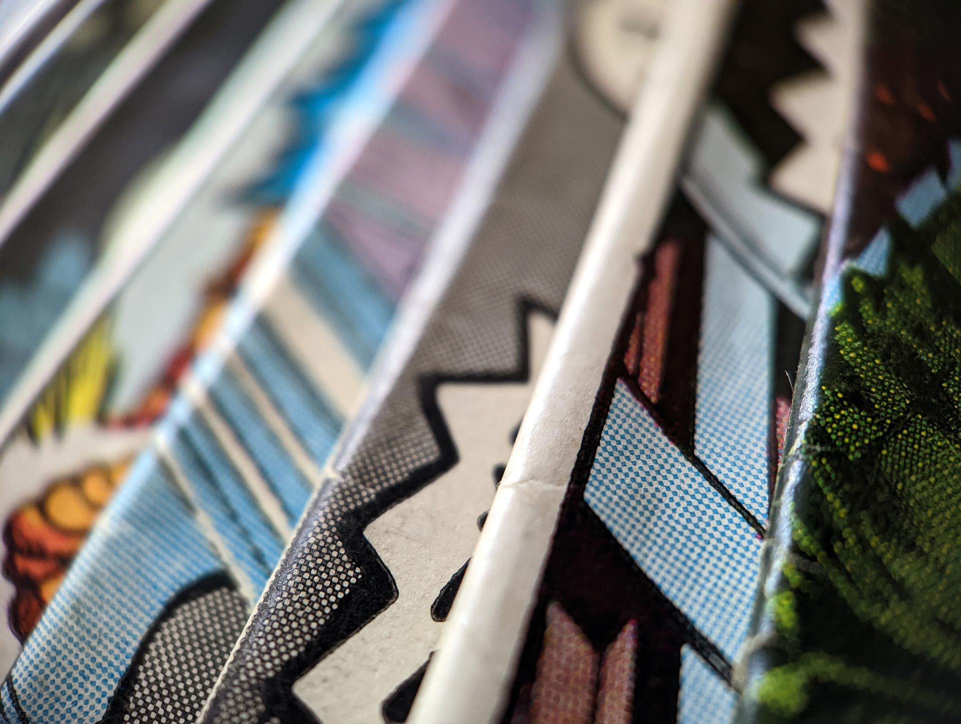 Close-up of comic book pages fanned out, showcasing colorful panels with speech bubbles and halftone dots.