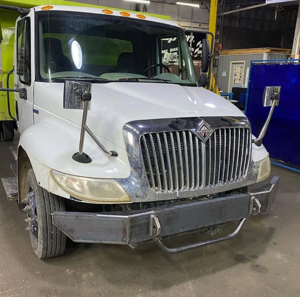 A white truck is parked in a garage next to a green truck.