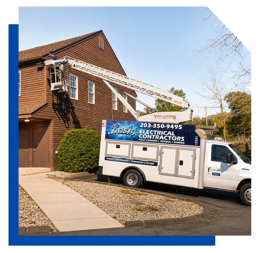 Electrician service van parked beside a brick building with a ladder on the roof under a blue sky