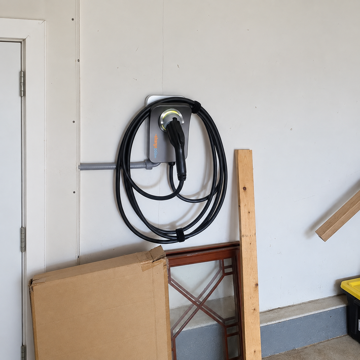 Wall-mounted hose reel with coiled black hose in a garage beside leaning cardboard and wood scraps