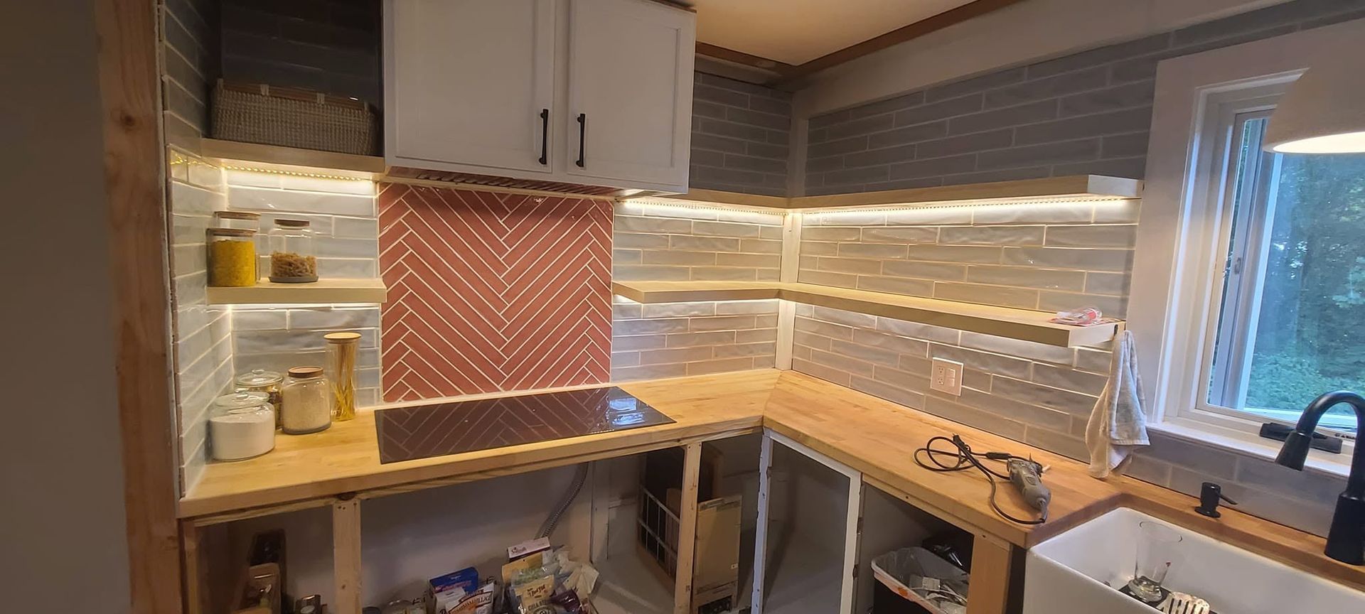 Modern kitchen corner with gray cabinets, orange backsplash, and a window over the sink.