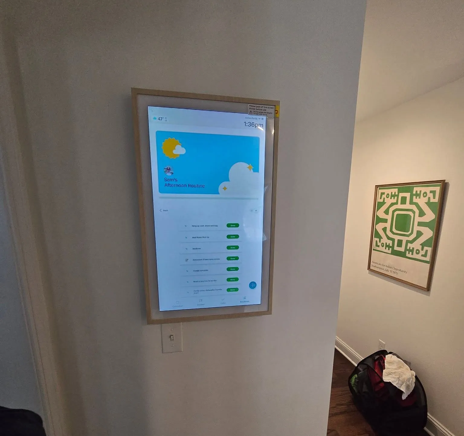 Wall-mounted framed digital display showing weather and forecast in a hallway near stairs