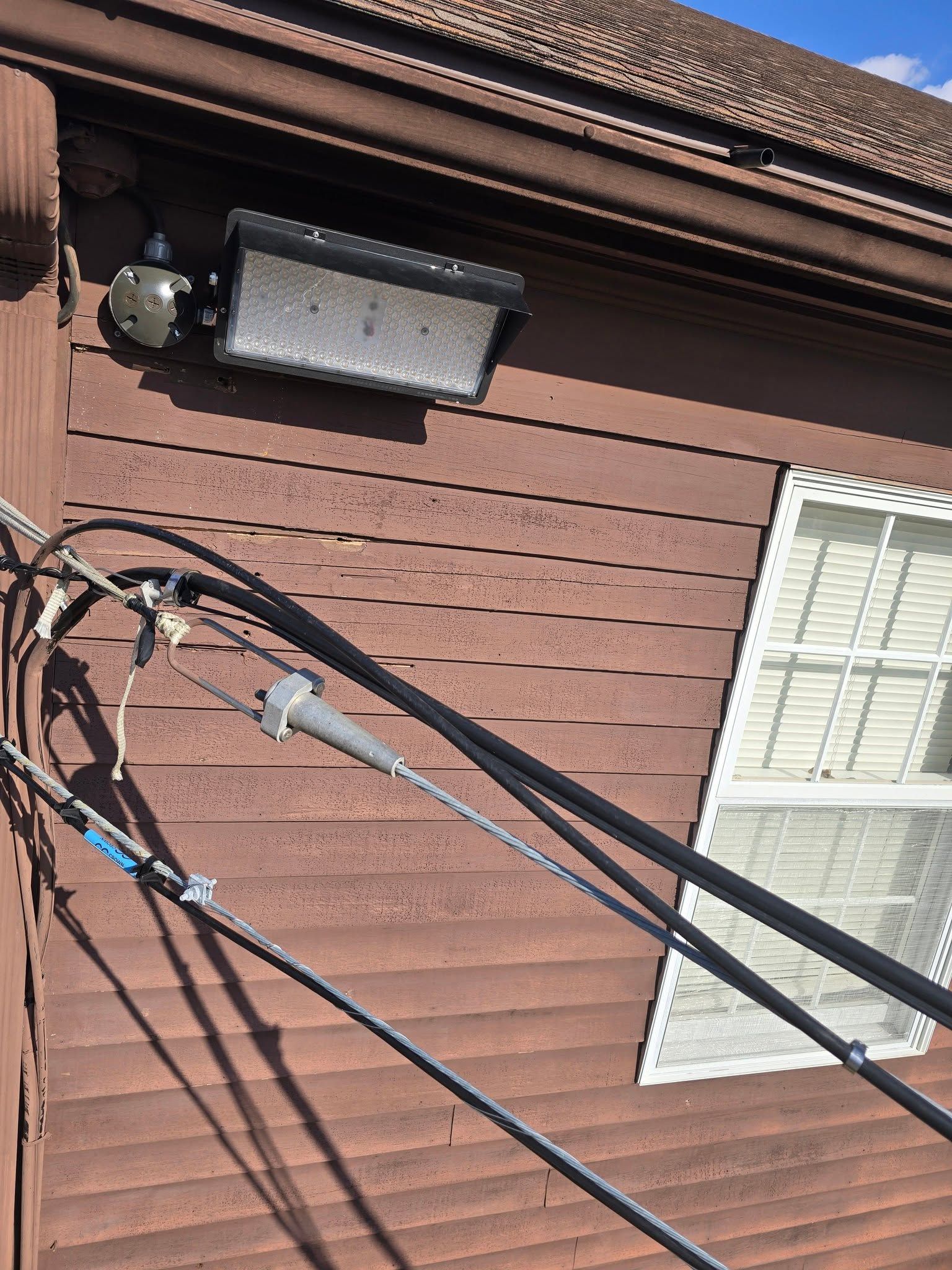 Brick house wall with outdoor light, window, and several cables crossing diagonally