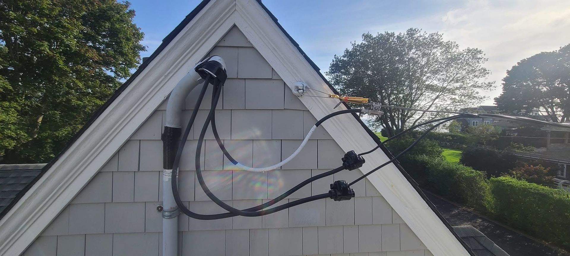 Electrical cables and conduit mounted on a small white house roof gable outdoors
