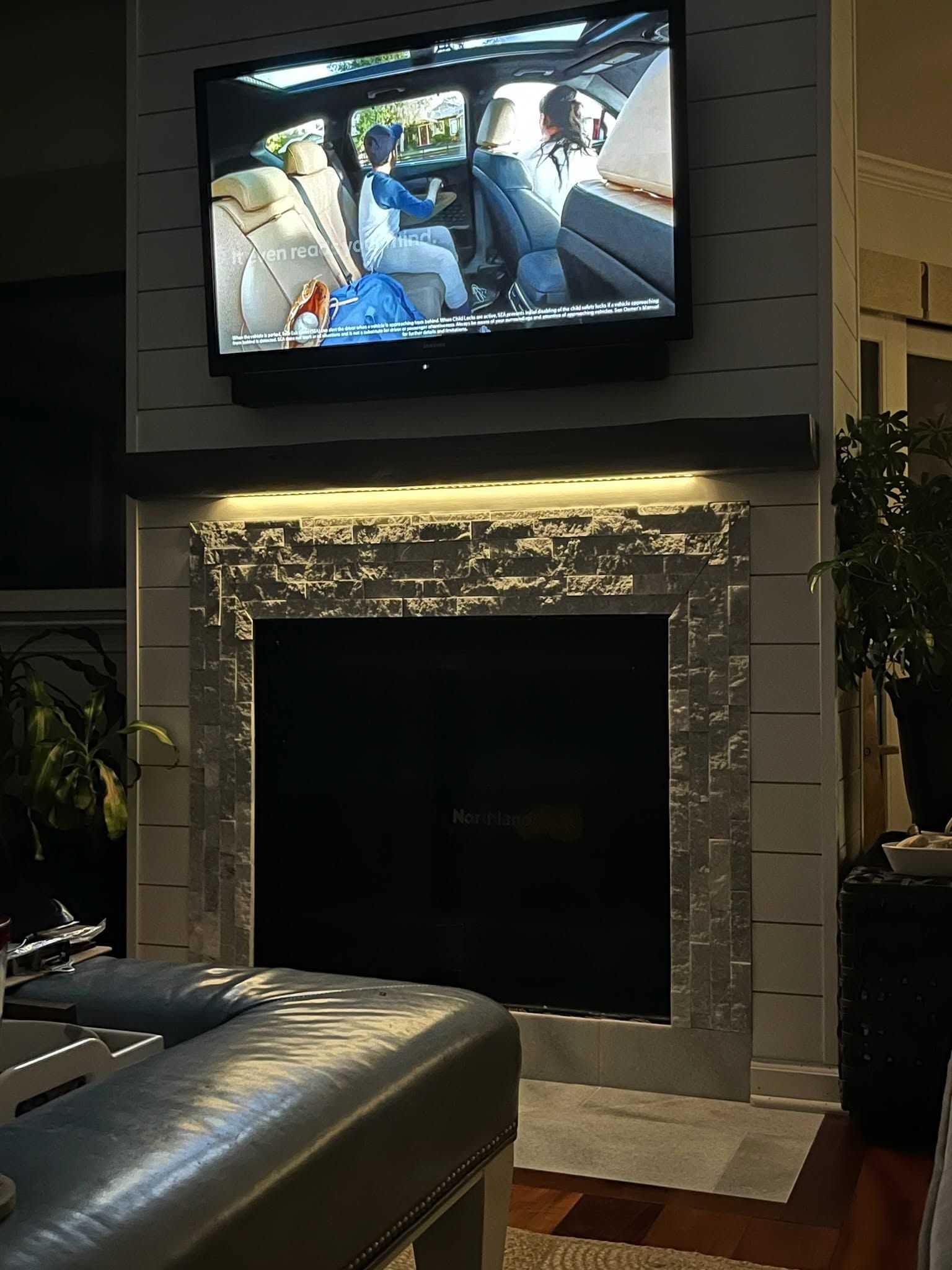 Living room with a wall-mounted TV above a stone fireplace and a leather sofa in the foreground