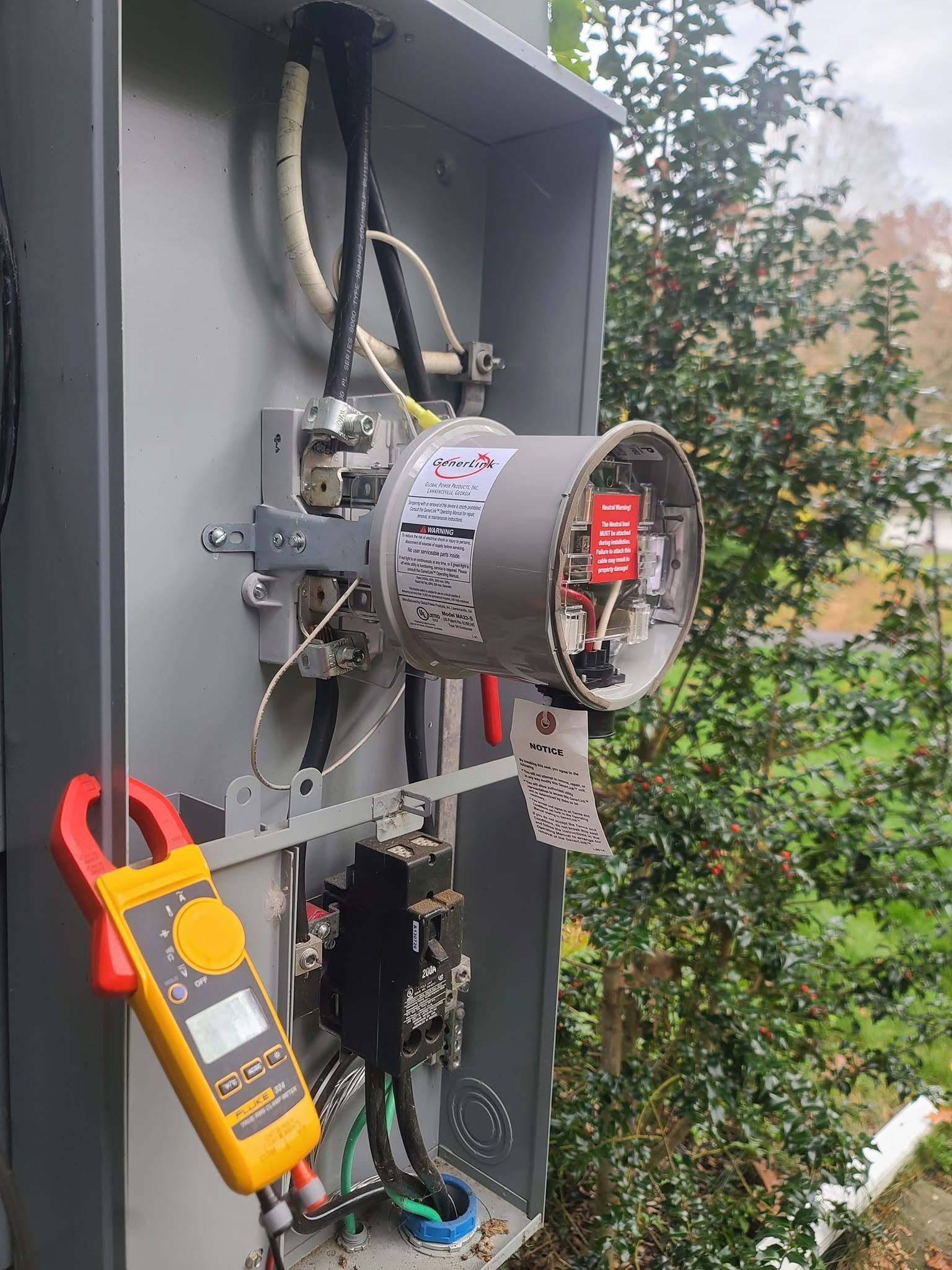 Open electrical panel with a motor and wiring; orange clamp meter hangs on the side.